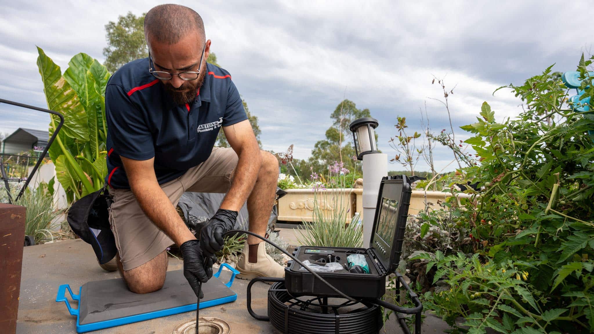 Person working on a roof with equipment, surrounded by plants and a cloudy sky.