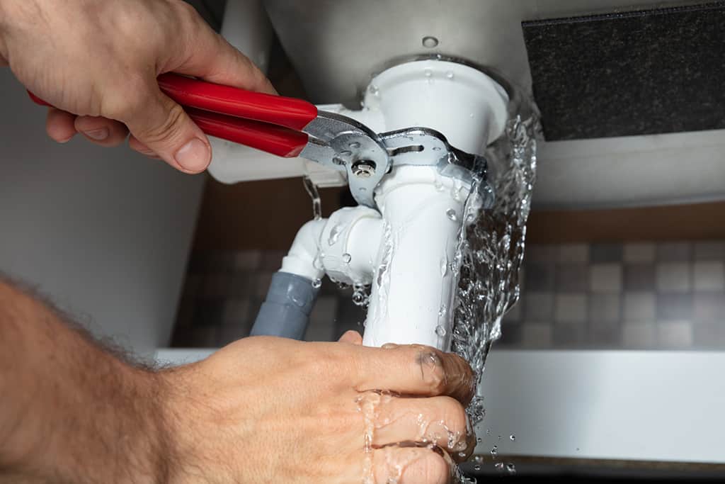 Person using pliers to fix a dripping faucet with water flowing.