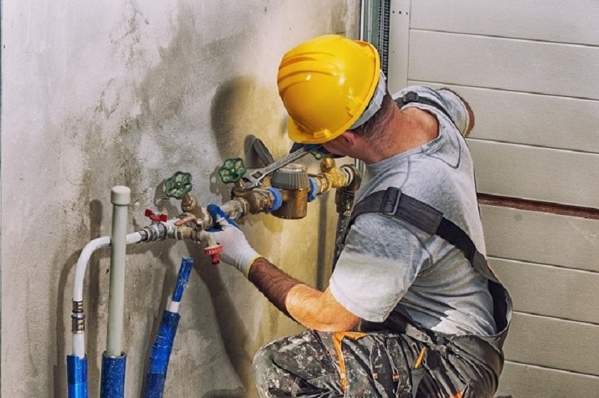 Person working on plumbing fixtures wearing a yellow hard hat and gloves.