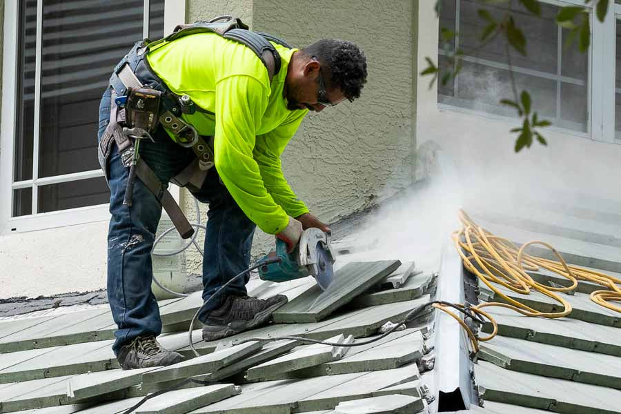 Worker in a bright yellow safety vest using a power tool on a roof.