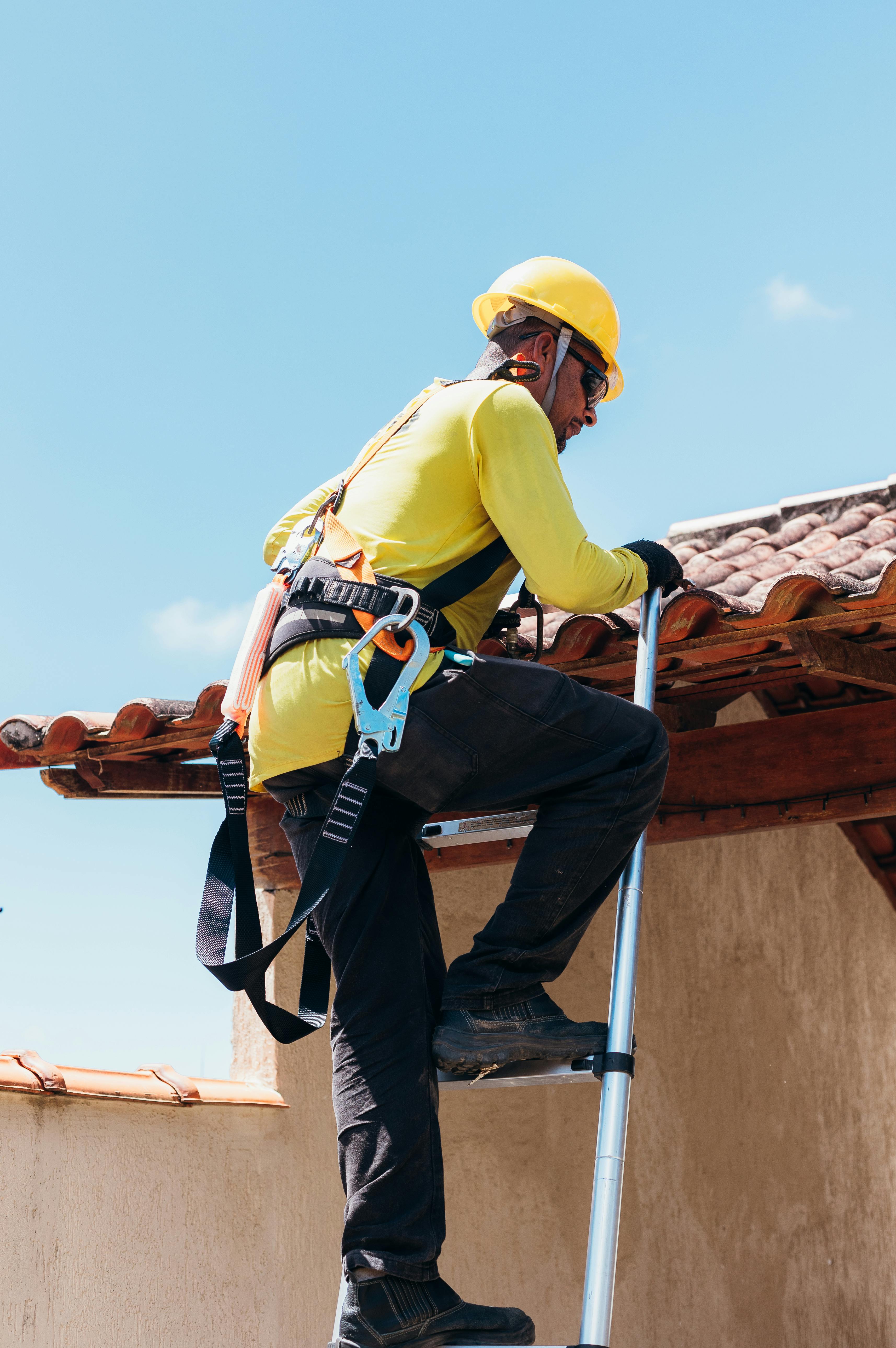 Person on a ladder wearing safety gear on a roof